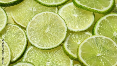 Overhead lime slices rotate in a horizontal frame, showing fresh citrus texture and layered detail.