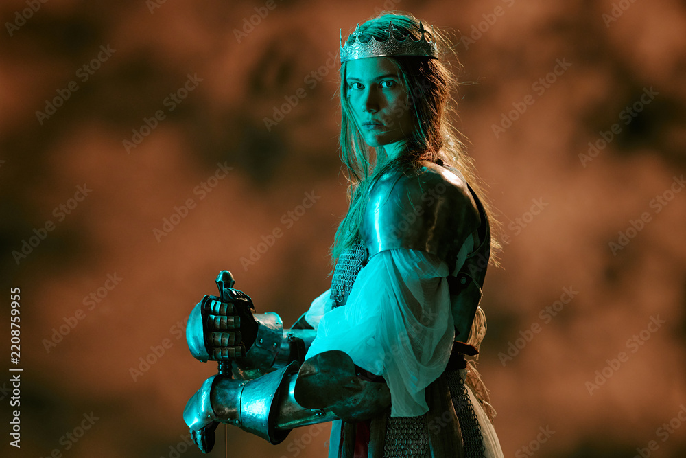 Obraz premium Portrait of young adult Caucasian woman wearing armor and crown holding sword representing leadership and power. Visual concept suitable for historical marketing