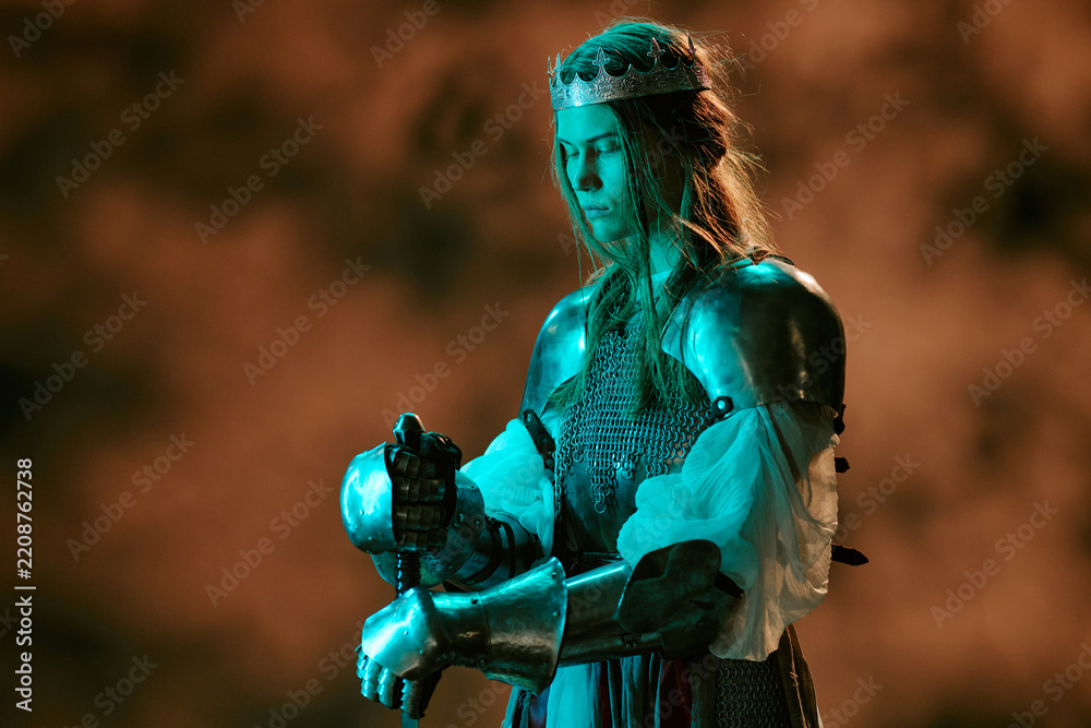 Obraz premium Caucasian young adult woman wearing armor and crown holding sword, symbolizing leadership and defense. Visual ideal for gaming promotion, book covers, entertainment marketing