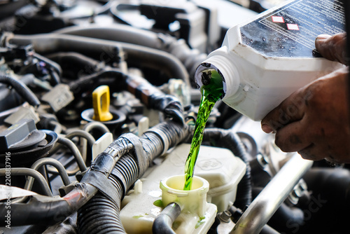 Mechanic adding green antifreeze liquid to a car engine during maintenance