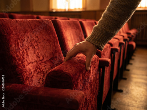 Empty theater seats with hand resting on red fabric armrest  