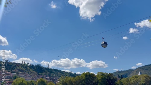 Cable car moving above a green mountain landscape under a bright blue sky. Scenic travel scene illustrating tourism, aerial transport, sightseeing and outdoor adventure.