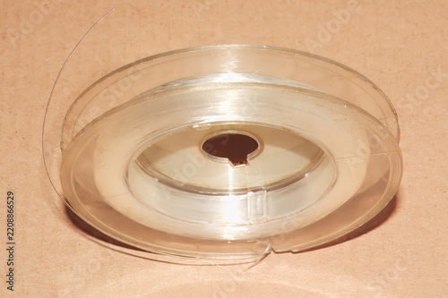 Clear plastic spool is coiled with fine, nearly invisible fishing line. The spool is set against a light brown backdrop.