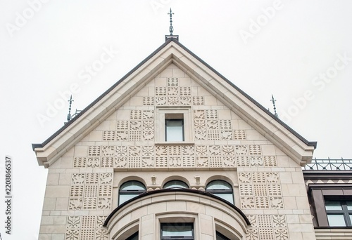 Image shows a detailed building facade featuring intricate carvings and geometric patterns, complemented by arched windows and a triangular roof.
