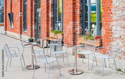Quaint outdoor café setting with metal chairs and tables against a rustic red brick building, adorned with window planters.