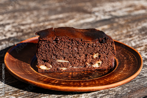 Slice of homemade chocolate cake on clay plate. Closeup of delicious piece of chocolate sponge cake or brownie with filling served on rustic ceramic plate over wooden table