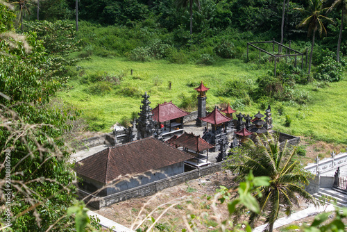 Balinese Hindu temple with tiered meru shrines and split gates set against a lush green hillside near Atuh Beach, Nusa Penida, Bali, Indonesia.