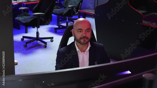 Bald businessman in a suit playing videogames at a gaming cafe