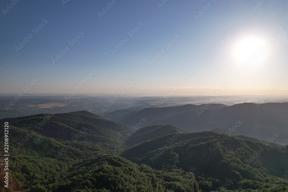 Obraz premium Drone panorama of bright morning sun over vast mountain ranges and hazy green valleys