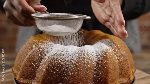 Baker sifting powdered sugar over baked bundt cake.