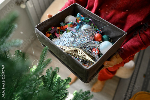 Woman holds a box of Christmas decor indoors to decorate the tree