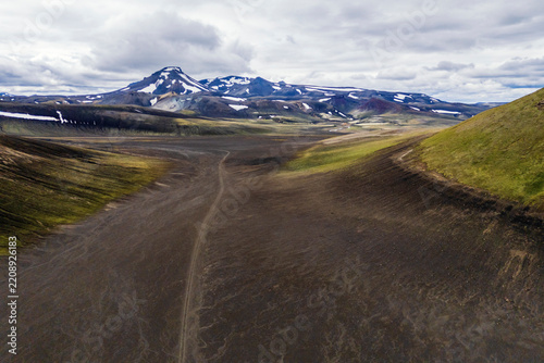 An unpaved dirt track winds through a volcanic valley in Iceland