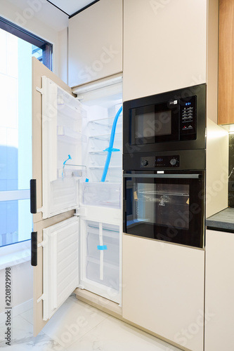 Open built in refrigerator beside oven and microwave tower in modern kitchen interior. Sleek apartment design with integrated appliances, minimalist cabinetry and premium storage concept