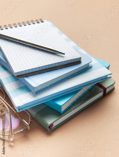 Stack of blue notebooks with pen and glasses