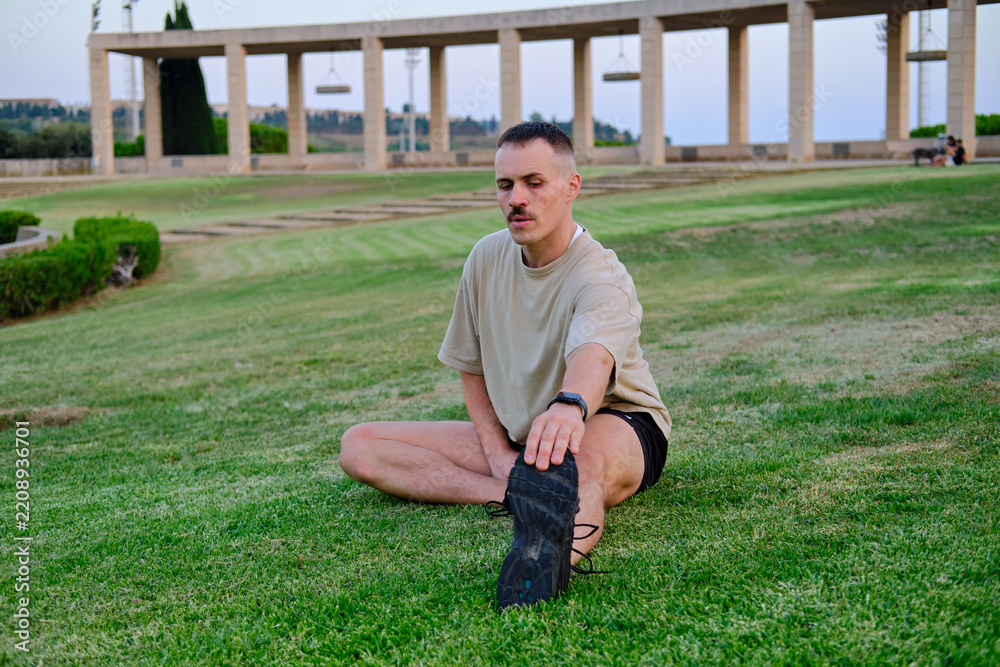 Fototapeta premium front view of Man stretching leg on grass in park