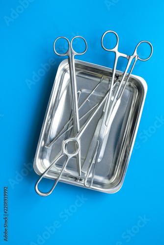 Sterile surgical instruments and tools - scalpels, scissors and others - in a stainless tray on blue background, top view