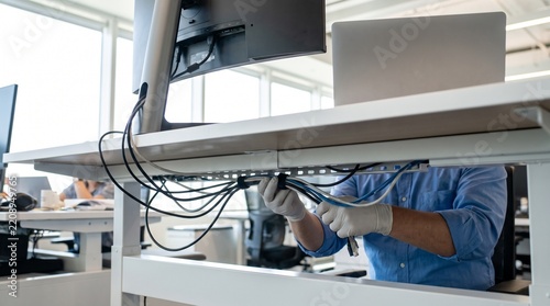 Technician wearing protective gloves organizing computer cables and wires under office desk for neat cable management and hardware maintenance setup   