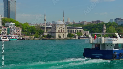 A beautiful cityscape of Istanbul featuring a magnificent historic mosque with tall minarets overlooking the turquoise Bosphorus sea with boats passing by on a sunny day