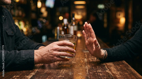 Extreme close-up of two friends hands at a bar counter as one offers an alcoholic drink while the other refuses with an open palm gesture, symbolizing responsible drinking, peer pressure, and personal