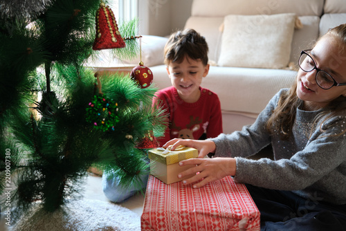 Happy children opening Christmas gifts near a decorated tree.