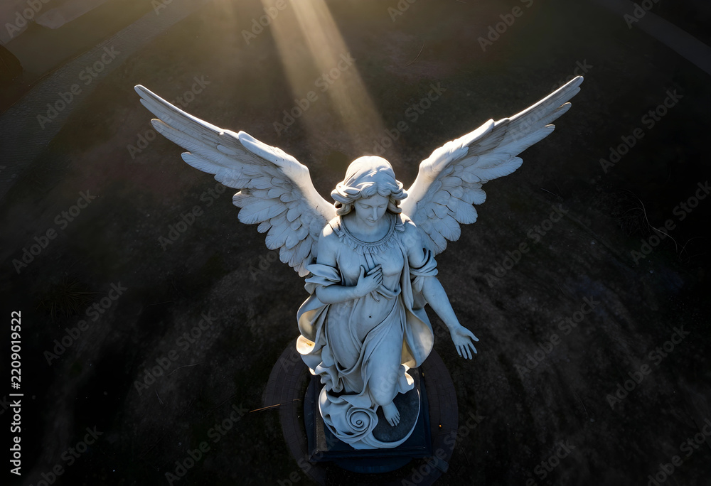 Fototapeta premium Spirituality and hope, marble angel statue with wings spread under divine light rays in a cemetery at sunset for religious and memorial concepts