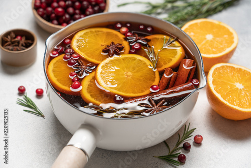 Hot mulled wine with cranberries, orange, rosemary, cinnamon and spices in a pot, Christmas winter drink on a light background with copy space