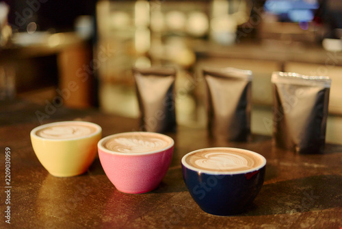 Fotografie Three ceramic cups filled with fresh latte art standing on counter near coffee bean bags