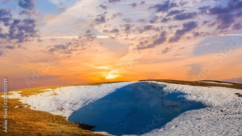 grass hill with melting snow at the sunset, spring outdoor evening time lapse scene