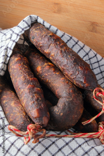 Close-up of homemade cured sausages or chorizo tied with red and white twine on a rustic wooden background. Vertical food photography.
