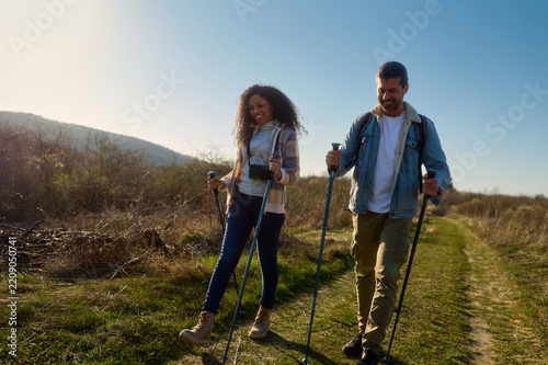 Fotografie Couple nordic walking with trekking poles along a sunny winding country trail, s