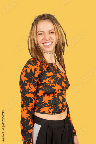 Young woman with dreadlocks smiling confidently on yellow background