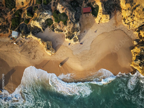 Drone top down view of Praia de Sao Rafael beach with a sandy cove, white surf, and rugged golden cliffs.