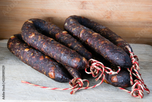 Rustic style food photography featuring dry sausages bound with red-white rope on a wood background.