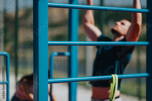 Fotografie Male athlete performing pull-ups on blue outdoor bars during a strength workout