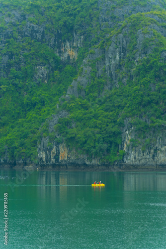 Tourists kayaking through an oyster pearl farm and lush green limestone mountain in Ha Long Bay, Vietnam