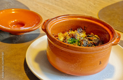 Hot meat dish served in a clay pot with baked potatoes or vegetables, sprinkled with herbs.