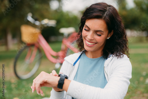 Woman checking fitness smartwatch after cycling in park