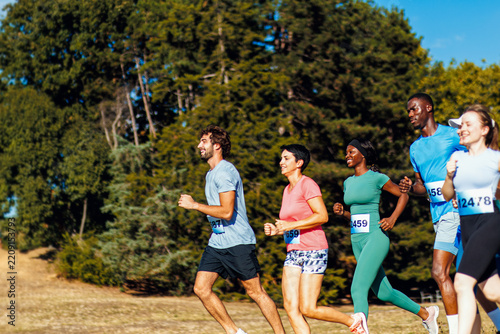 Group of smiling runners competing in outdoor marathon race in park.