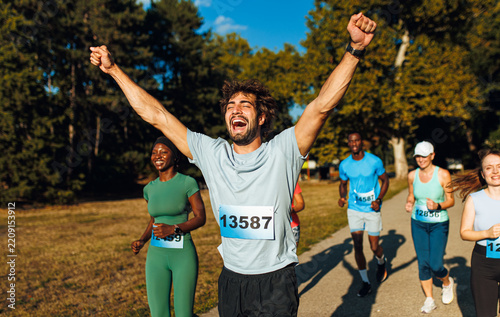Ecstatic male runner celebrating with arms up while crossing marathon finish line.