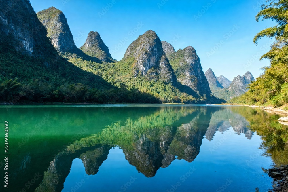 Fototapeta premium Serene mountain landscape with clear lake reflecting karst peaks under blue sky