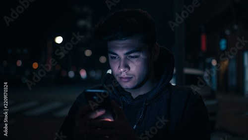 Obraz na płótnie 夜の街でスマートフォンを見つめる若い投資家