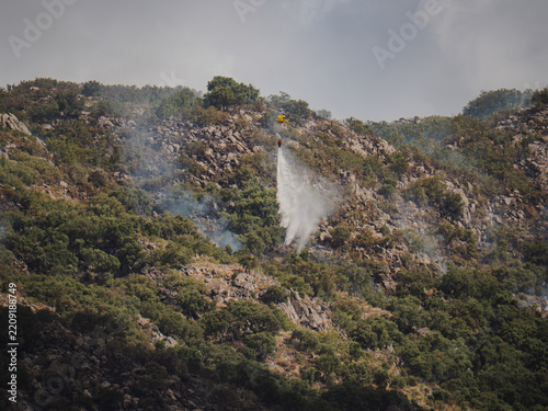 Firefighting helicopter perform water drop over hillside wildfire