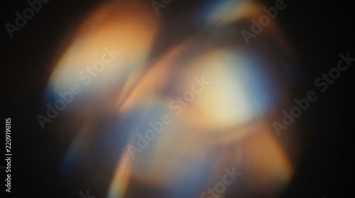 Abstract blurred light leak overlay texture with glowing warm orange and soft blue optical lens flare on dark background
