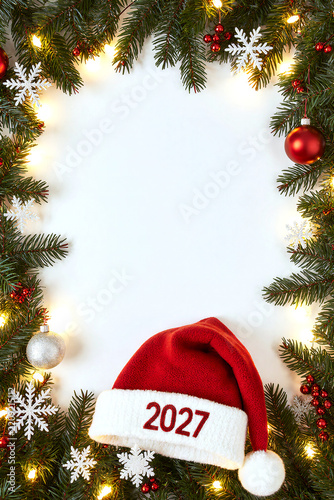 Christmas frame with evergreen branches, glowing lights, ornaments, snowflakes, and red Santa hat marked 2027 around white center