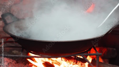 Close up shot of roasting coffee beans in large pan over traditional open wood fire with smoke.
