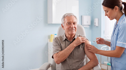 Senior man receives a vaccination from a nurse while seated in a medical clinic, illustrating immunization, preventive care and healthcare for older adults.