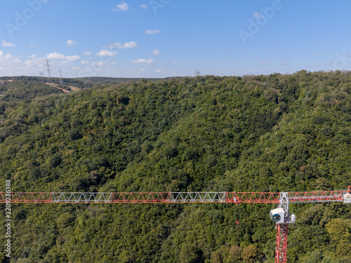 Aerial view of a red and white construction crane jib extending over a dense green forest under a clear blue sky in Istanbul, Istanbul, Turkiye.