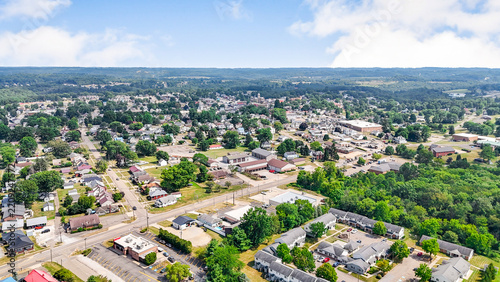 Suburban town aerial view photo. Extensive small town landscape with residential homes local businesses and green trees under a blue sky with white clouds