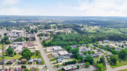 Aerial view of a quiet suburban town landscape. Small residential houses and local commercial buildings nestled between lush green forests. Sunny daylight atmosphere for real estate