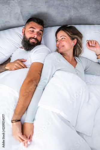 Young loving couple is sleeping in their bed. They are holding hands and enjoying good sleep.
